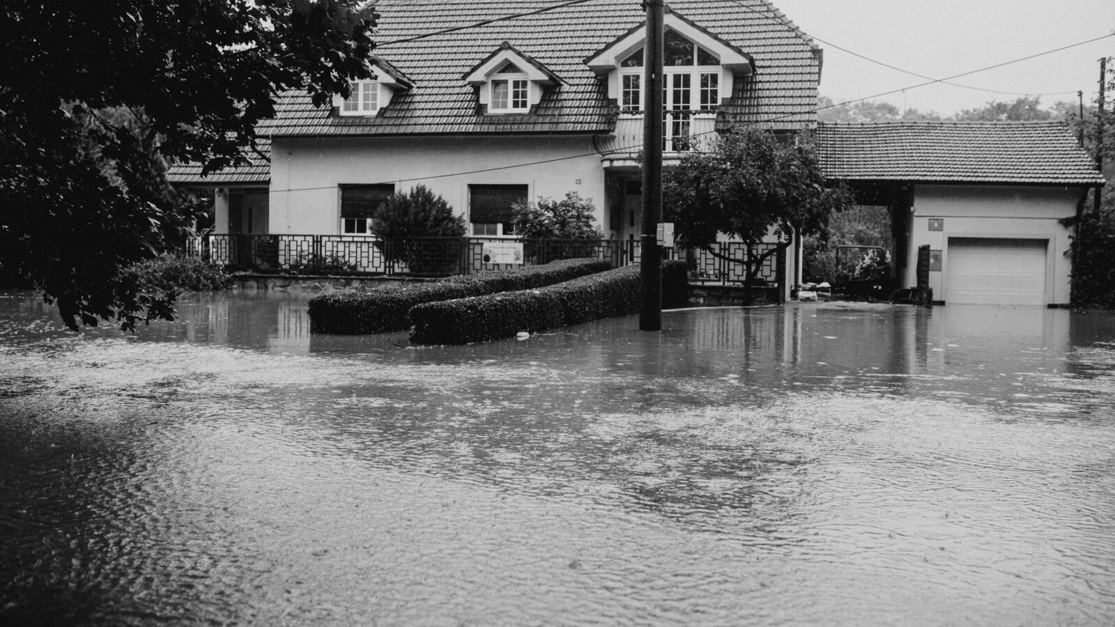 Casa de un barrio residencial rodeada por agua tras una inundación, en blanco y negro